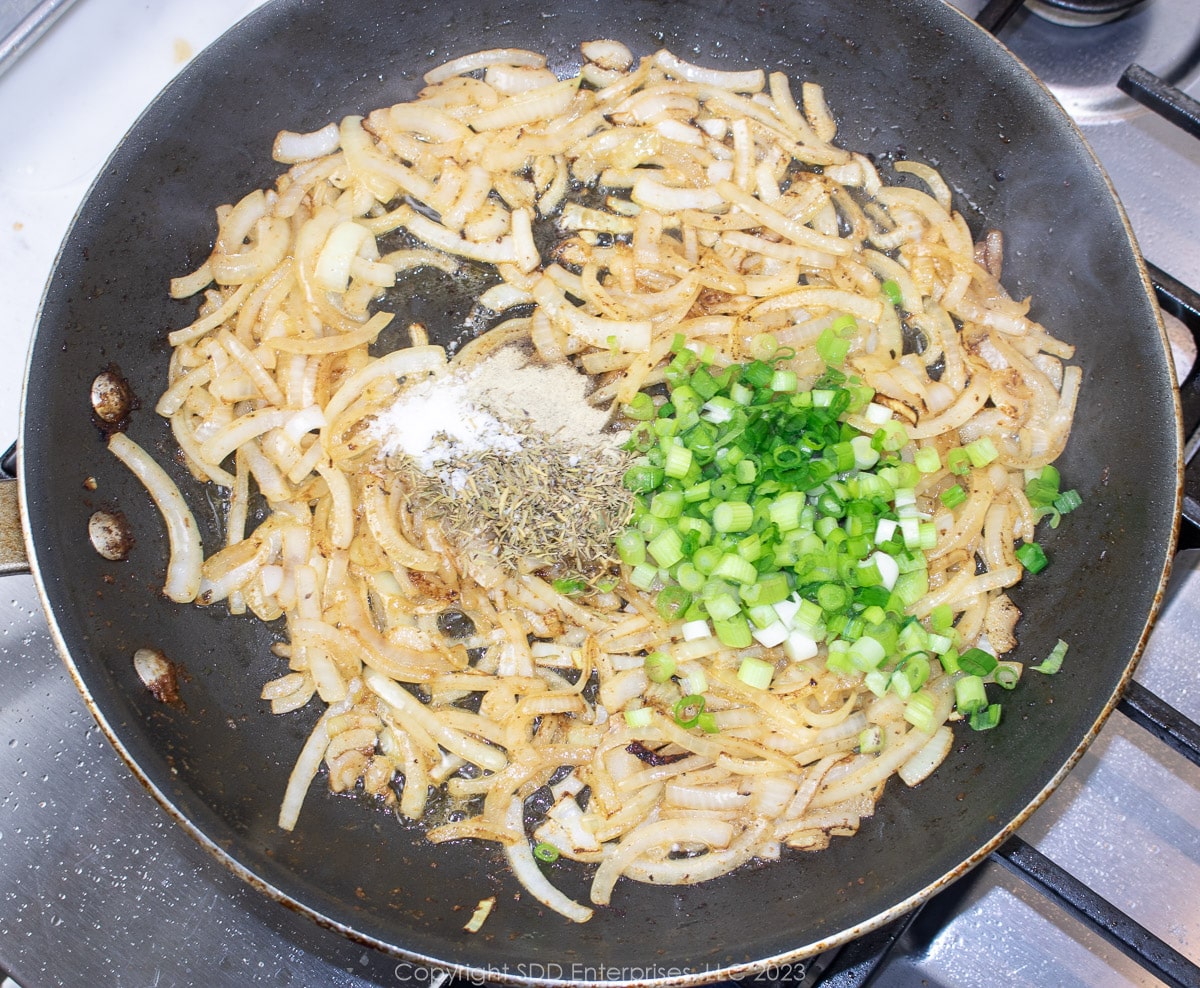 Green onions and seasonings added to onions in a  saute pan