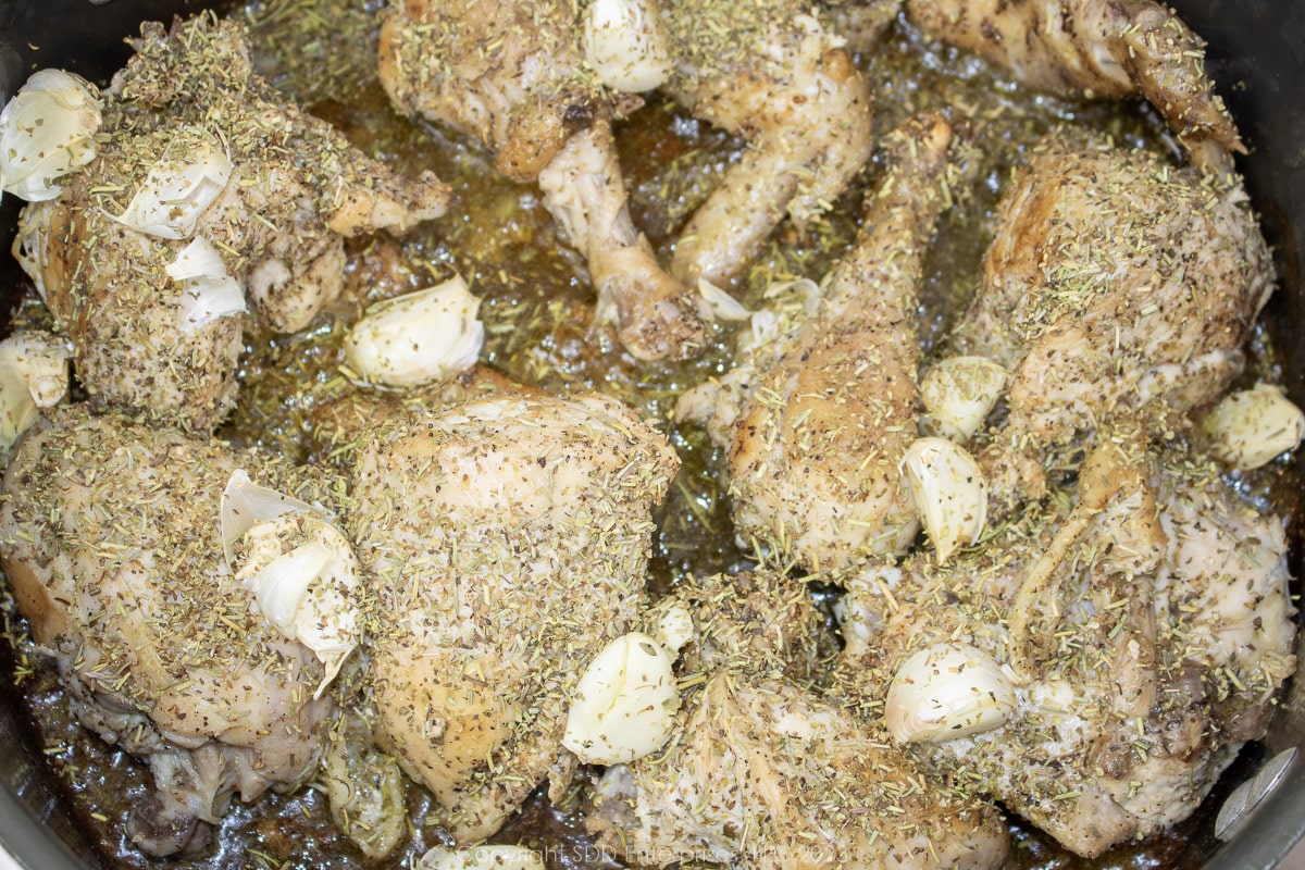 Browned chicken pieces seasoned with garlic cloves and herbs.