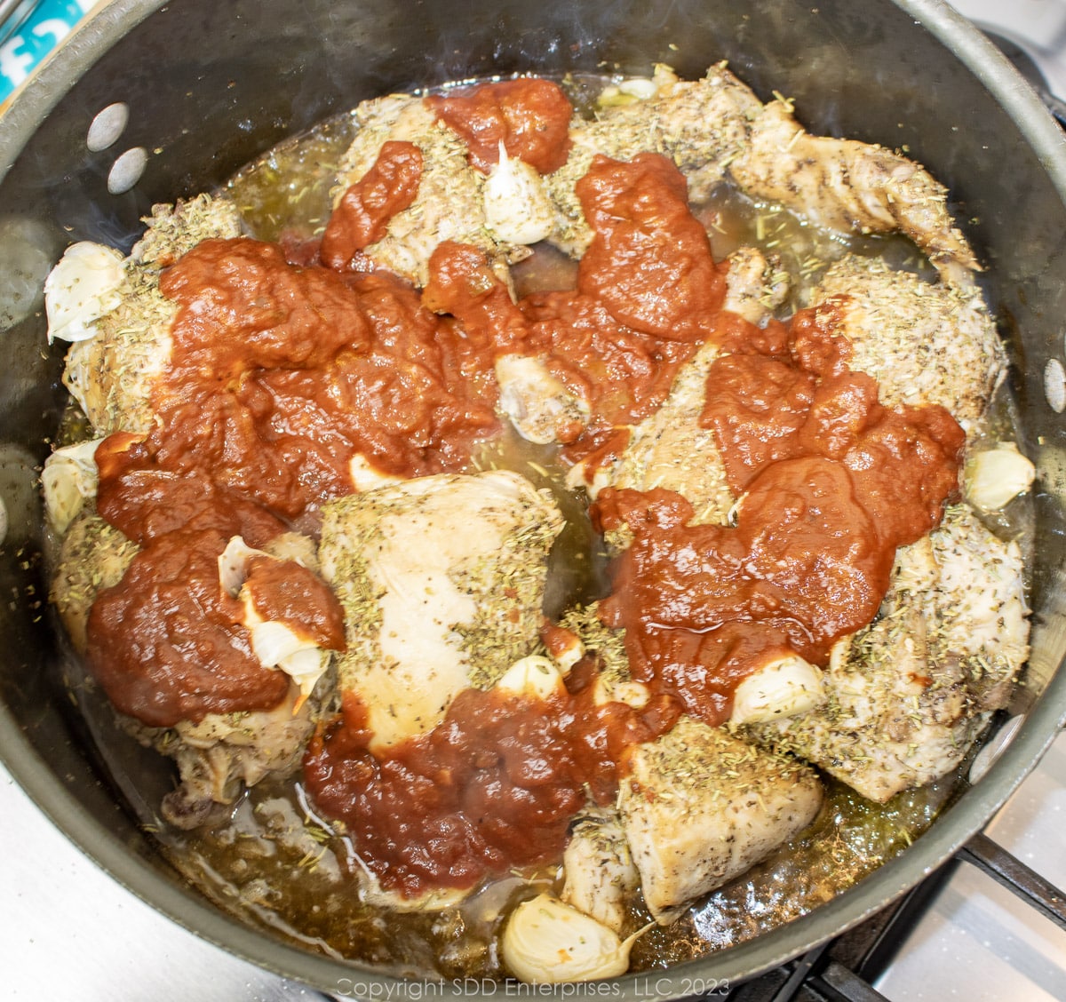 White wine and Red Gravy added to seasoned chicken pieces in a Dutch oven.
