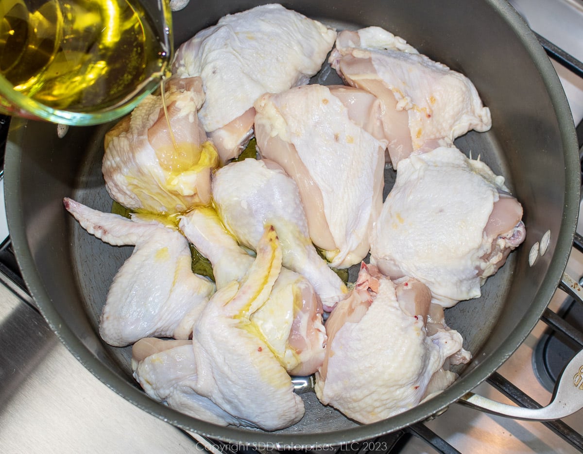 Pouring olive oil over cut up chicken in a Dutch oven.