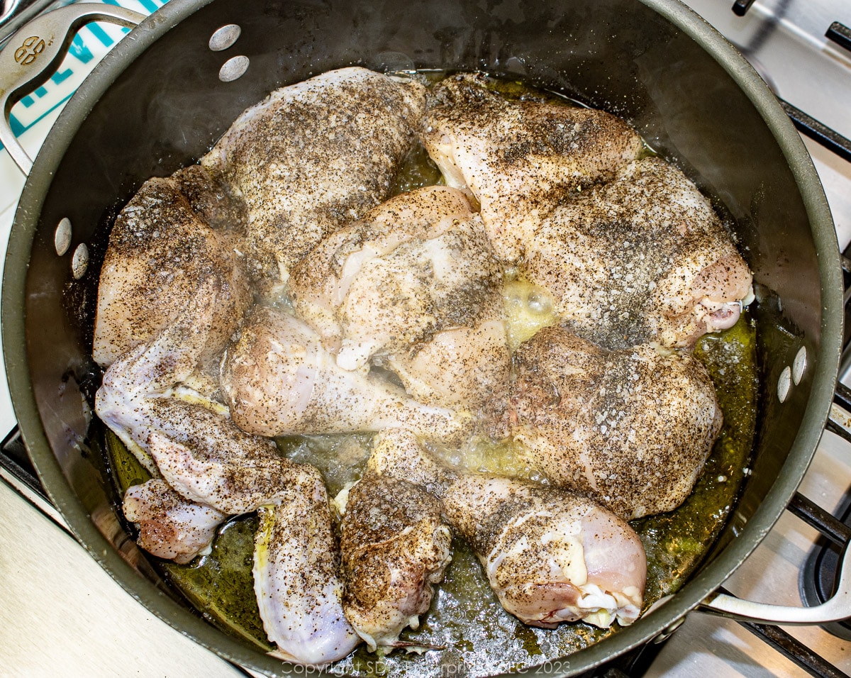 Seasoned chicken pieces being browned in a Dutch oven.