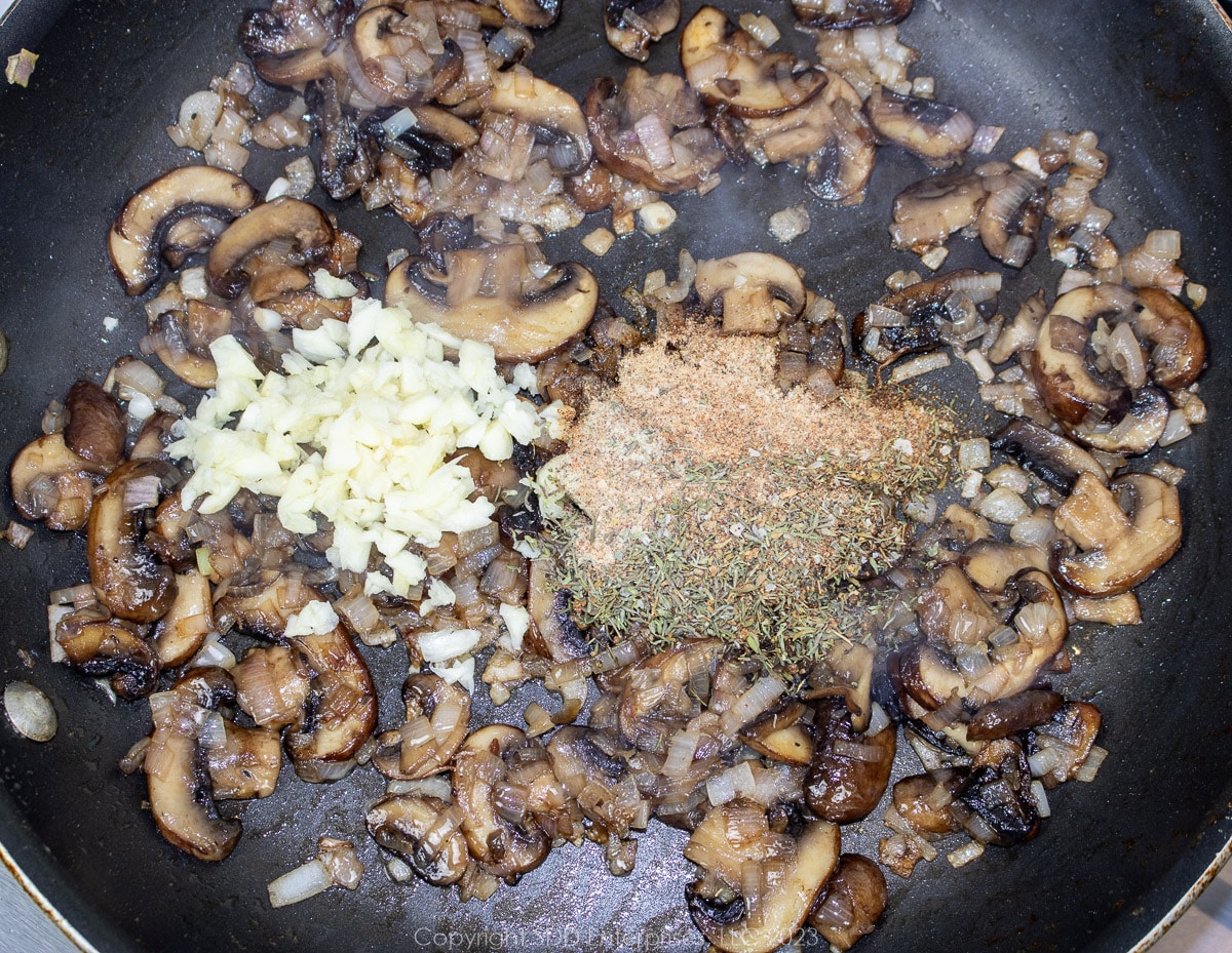 chopped garlic and herbs and spices added to sautéed mushrooms in a skillet.