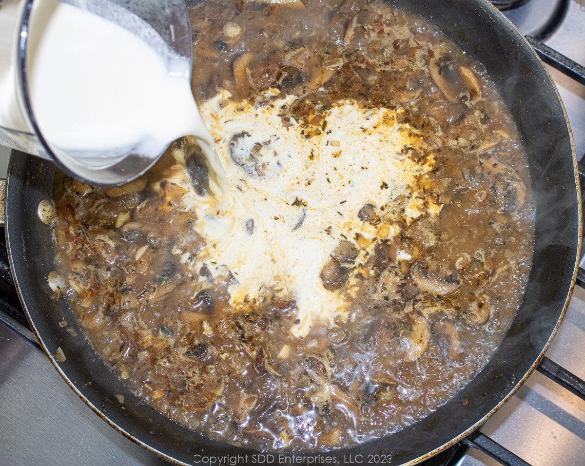 heavy cream being added to reduced liquids and mushrooms in a skillet.