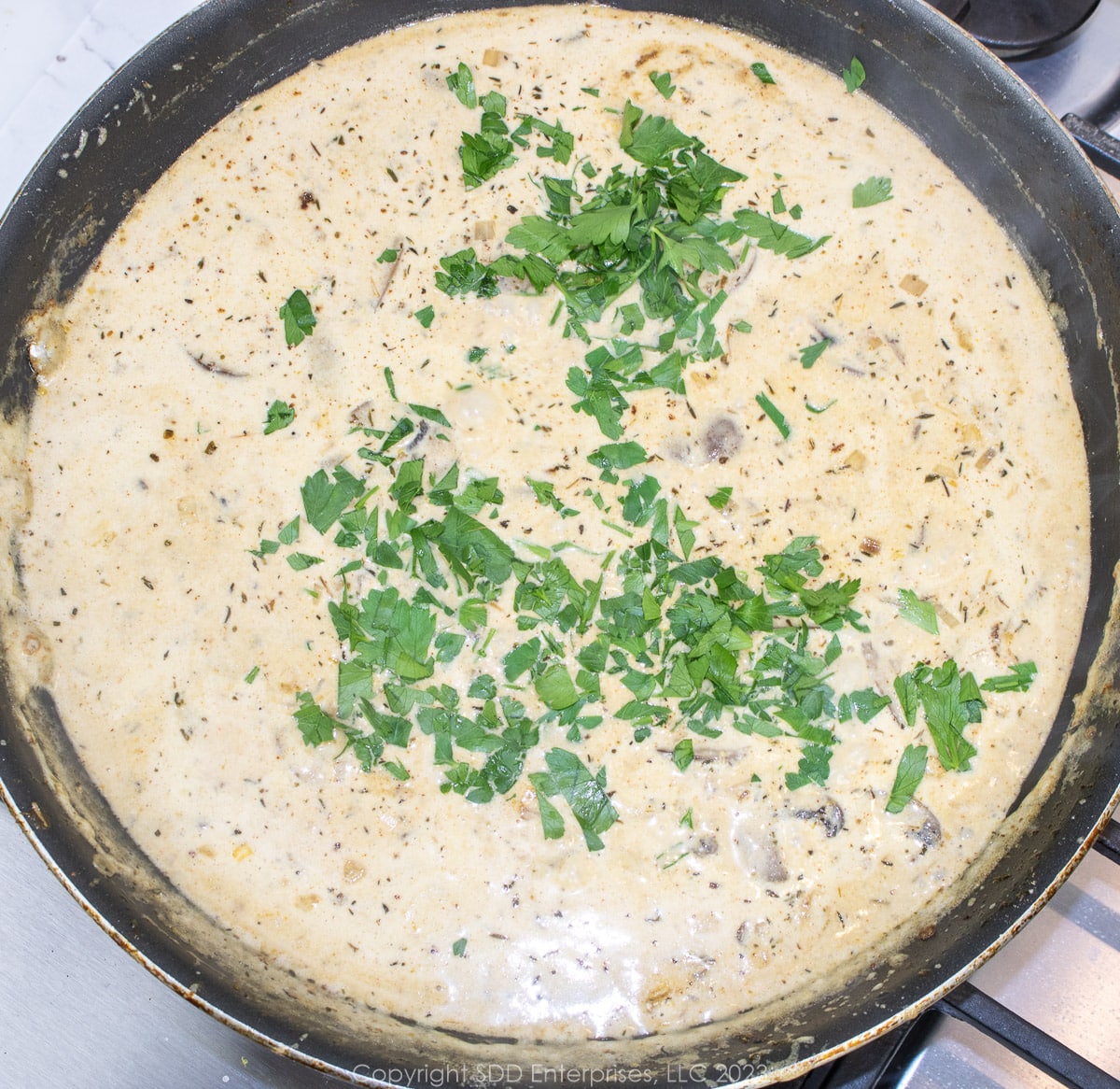 parsley added to a cream sauce in a skillet.