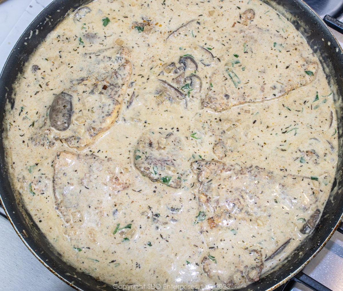 sautéed chicken breasts simmering in a cream sauce in a skillet.
