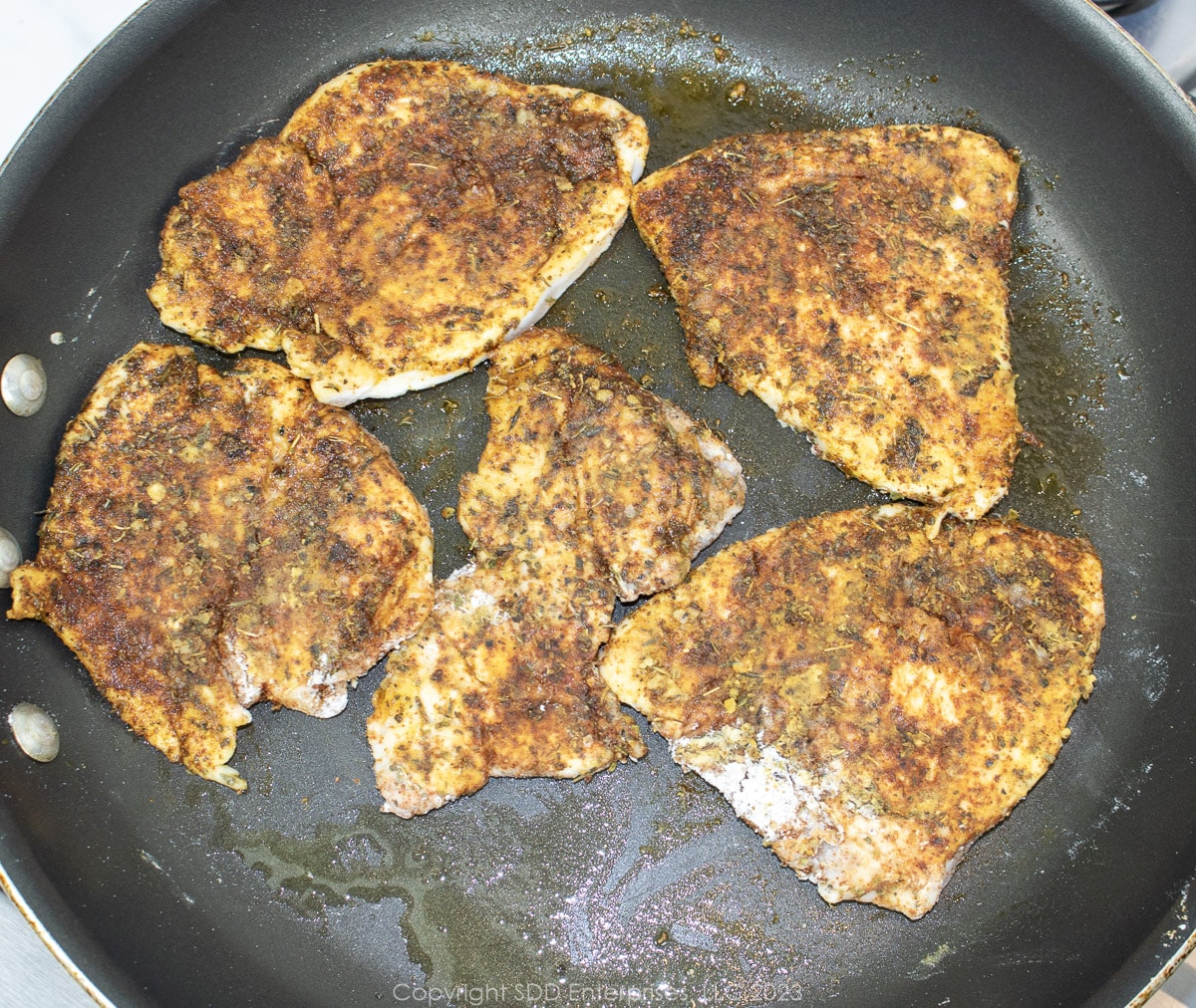 Chicken breasts sautéing in a skillet.