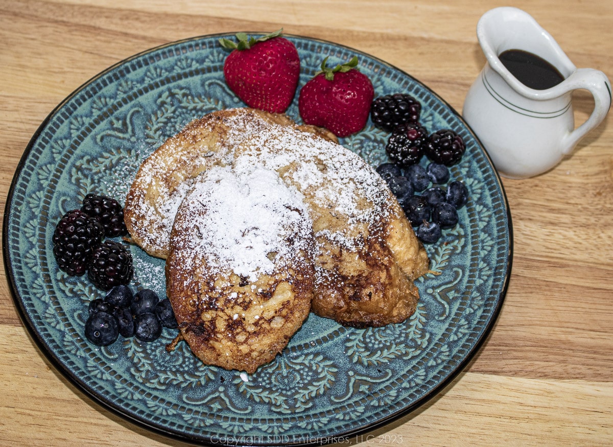 Pain Perdu or French Toast on a blue green plate with powdered sugar and fruit garnish.
