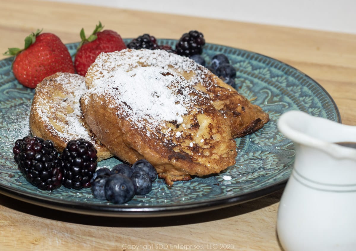 Slices of Pain Perdu or French Toast on a blue-green plate with powdered sugar and fruit garnish.