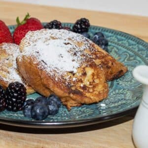 Pain Perdu (French toast) on a blue green plate with fruit garnish and powdered sugar.