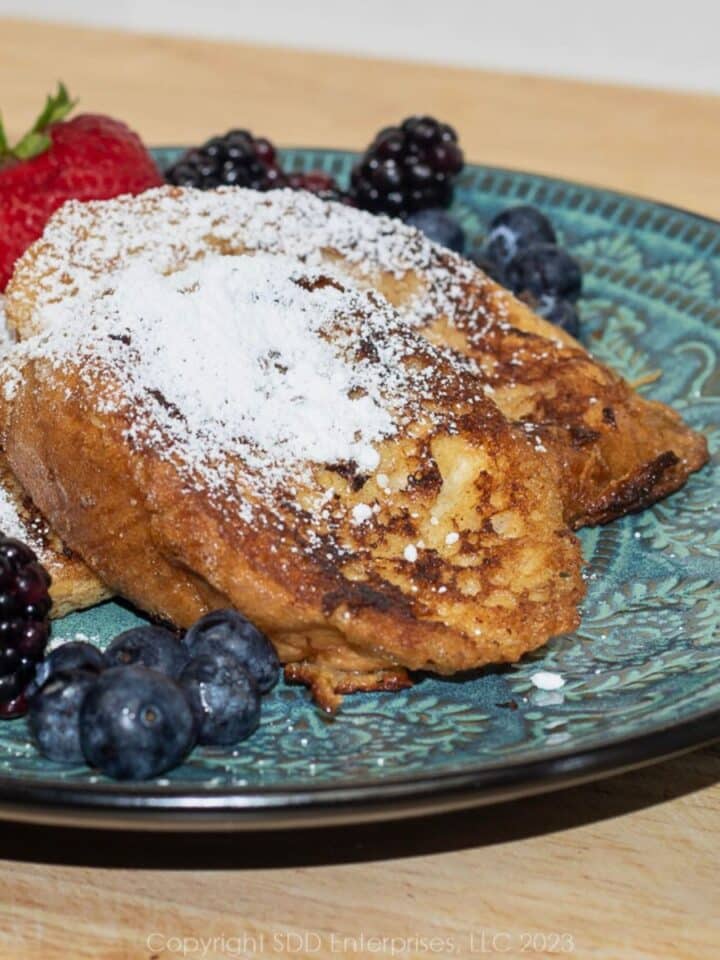 Pain Perdu (French toast) on a blue green plate with fruit garnish and powdered sugar.