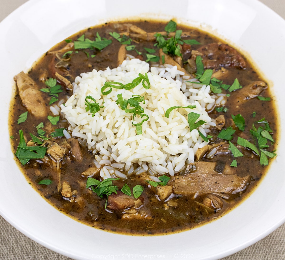 A bowl of Chicken and Andouille Gumbo with white rice and garnish. 