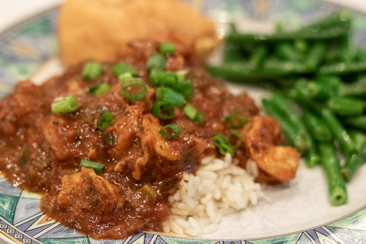 Shrimp Creole over rice with green beans and a roll on a blue-green dish