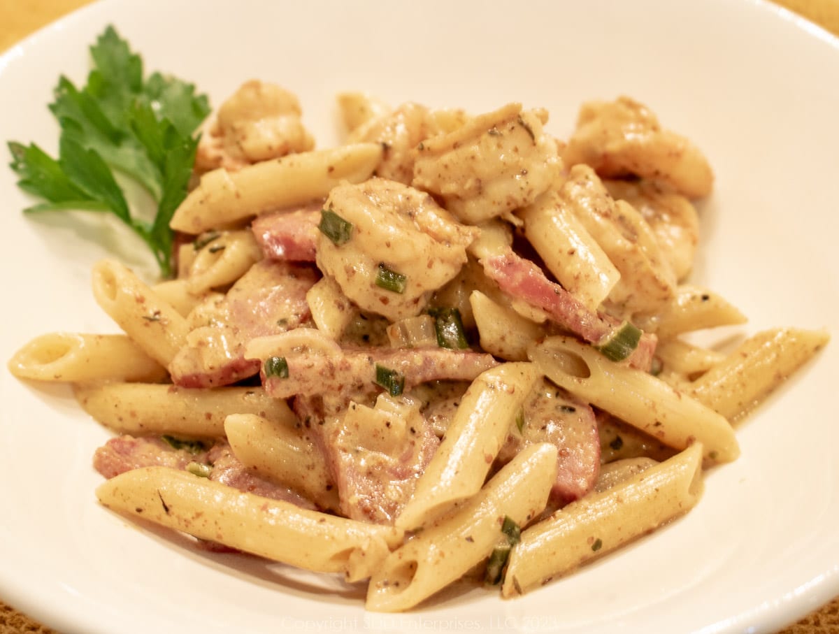 Shrimp and Andouille in a creamy creole mustard sauce in a white bowl with garnish.