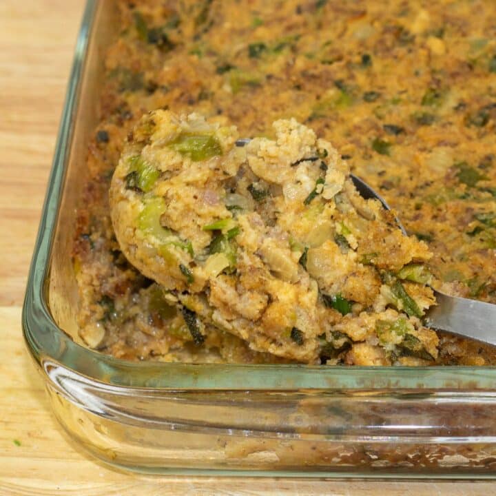 Cornbread Dressing with Sausage in a glass baking dish with a serving spoon.