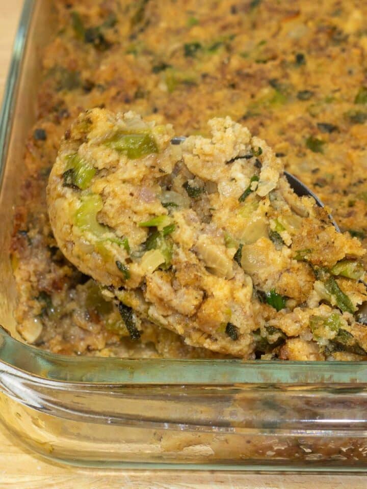 Cornbread Dressing with Sausage in a glass baking dish with a serving spoon.