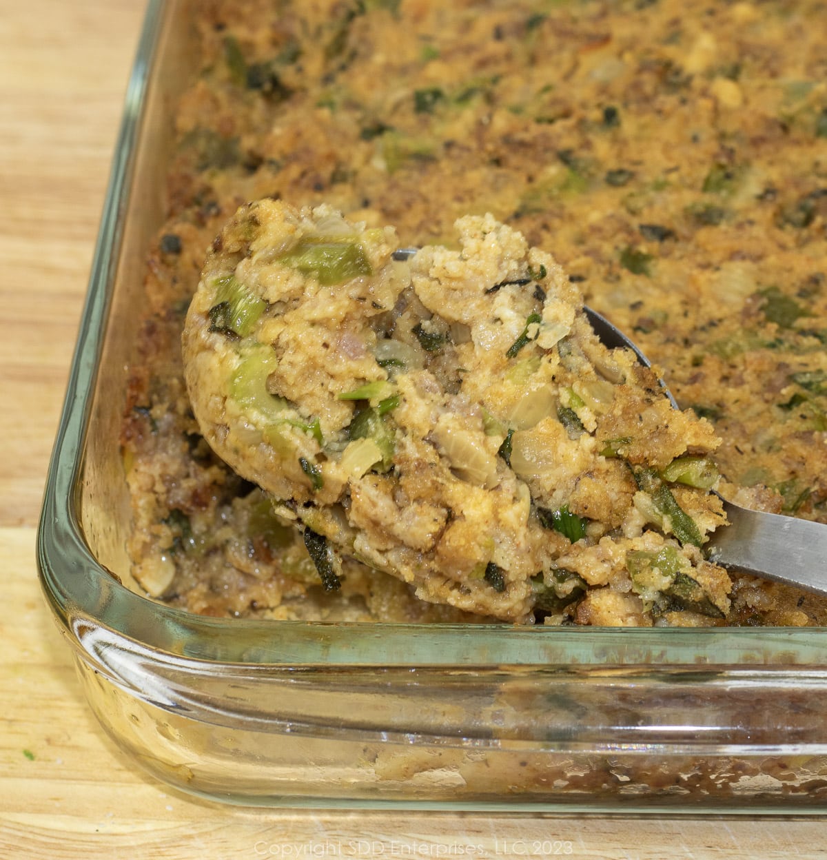 Cornbread Dressing with Sausage in a glass baking dish with a serving spoon.