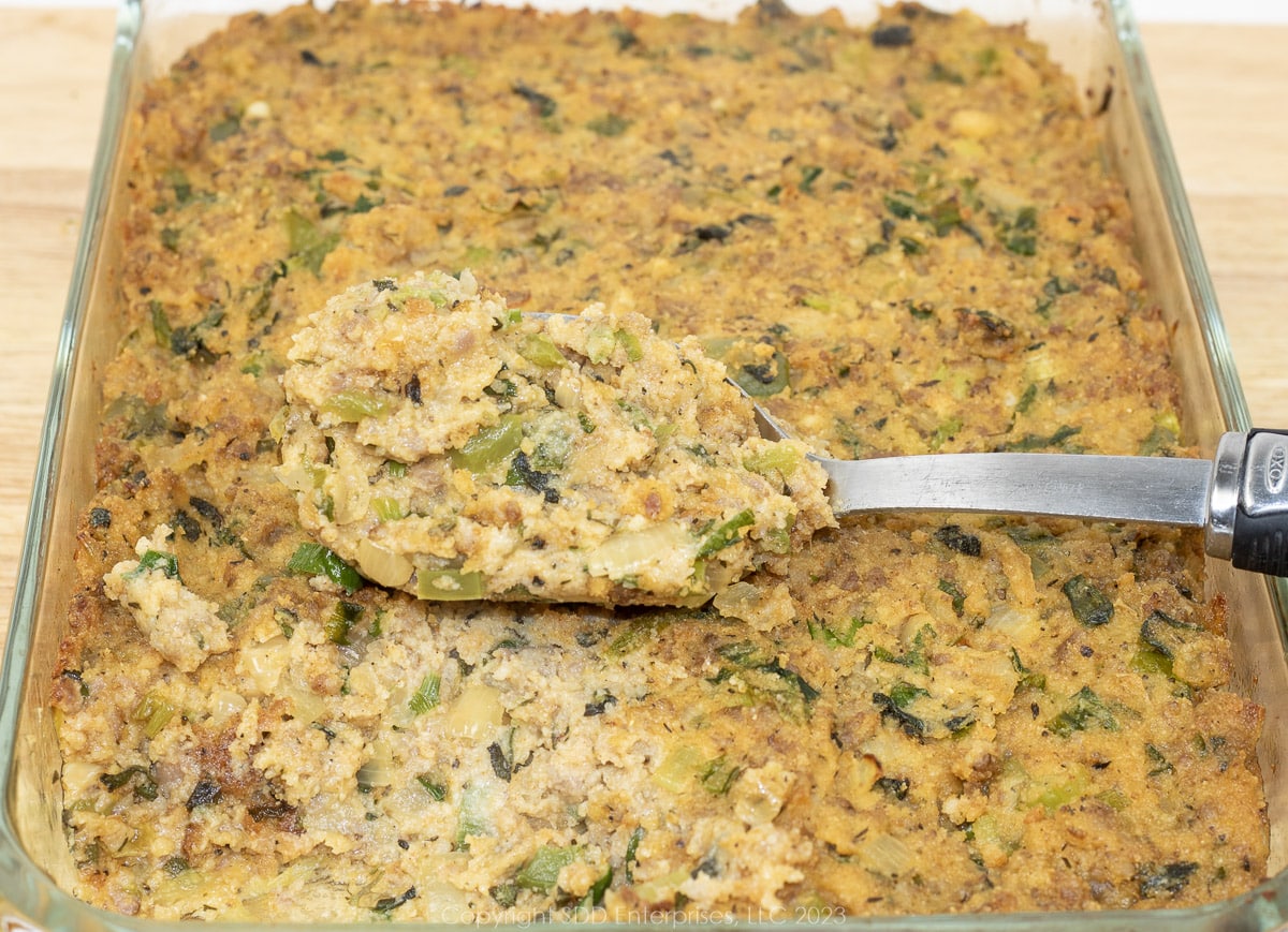 Cornbread Dressing in a glass baking dish with a serving spoon.