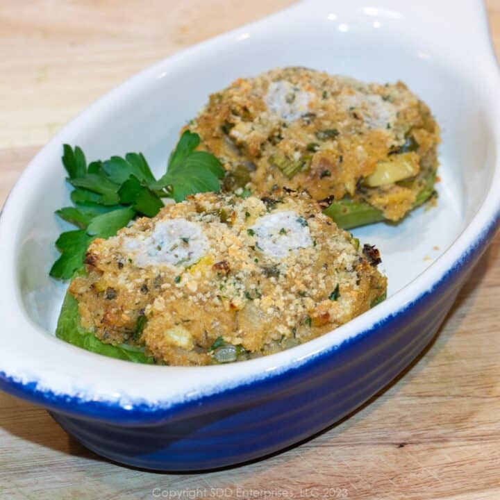 Two stuffed mirlitons in a serving dish with garnish.