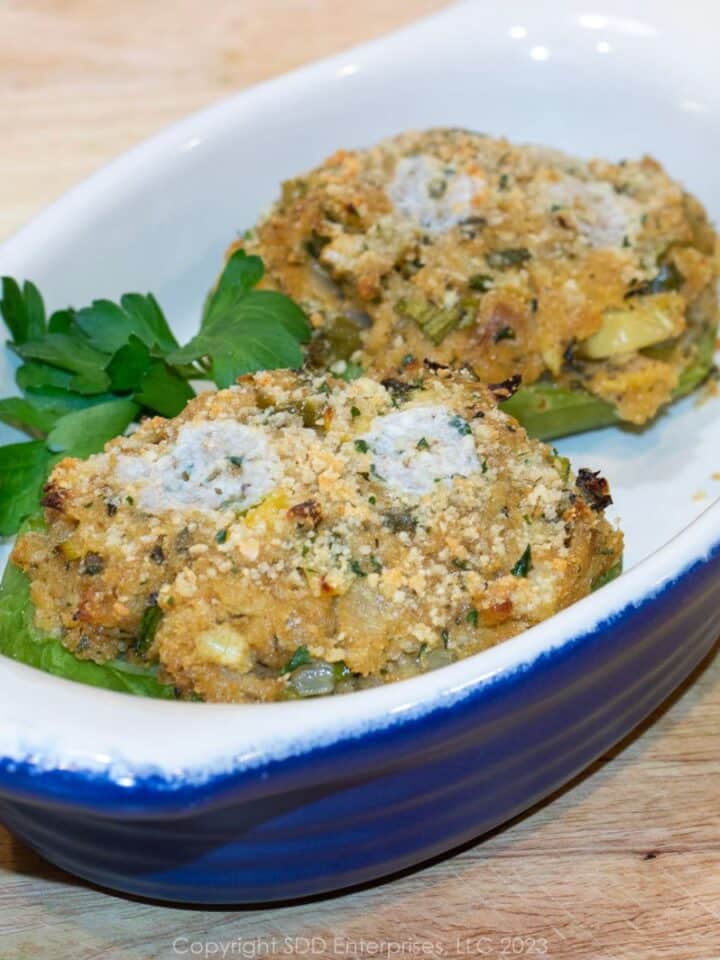 Two stuffed mirlitons in a serving dish with garnish.