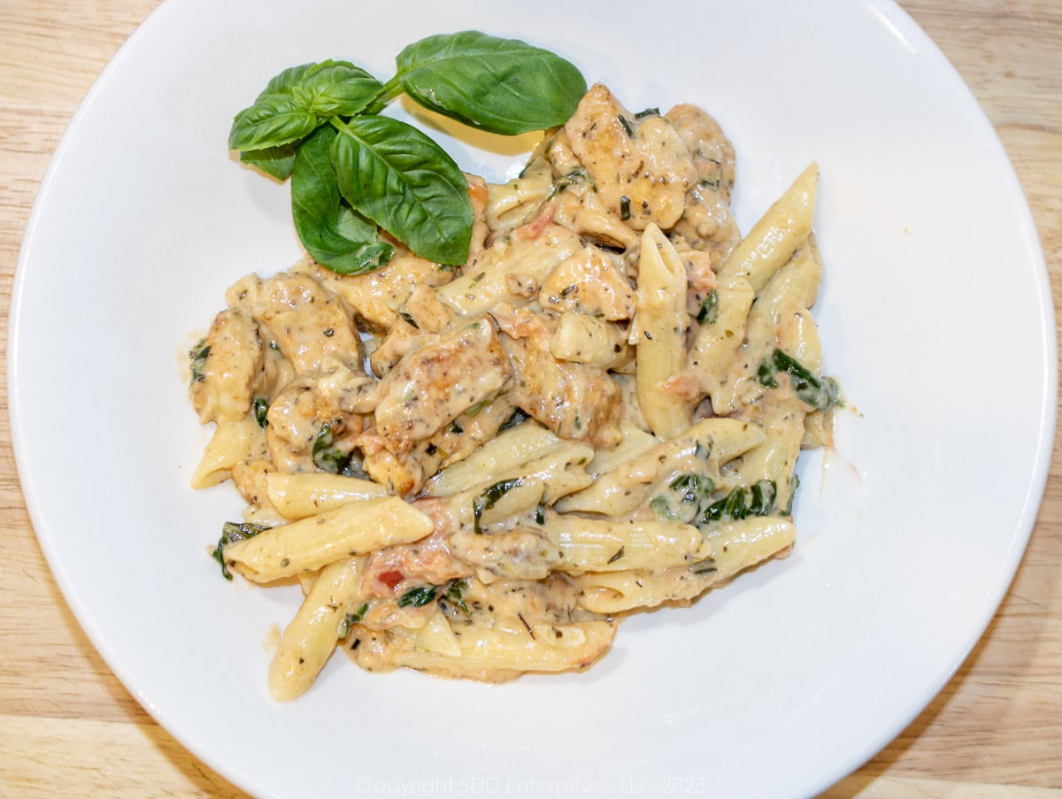 Creole Chicken Florentine mixed with penne pasta and garnish on a white serving dish.