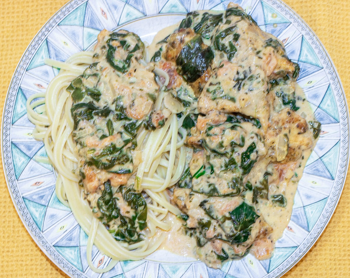 Creole Chicken Florentine with linguine on a blue green serving plate.