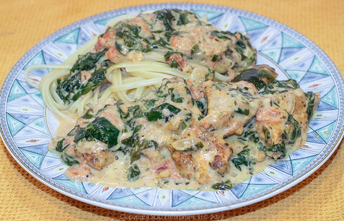 Creole Chicken Florentine served with pasta on a blue green dish.