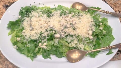 green salad with romano cheese on a serving platter with serving tongs.