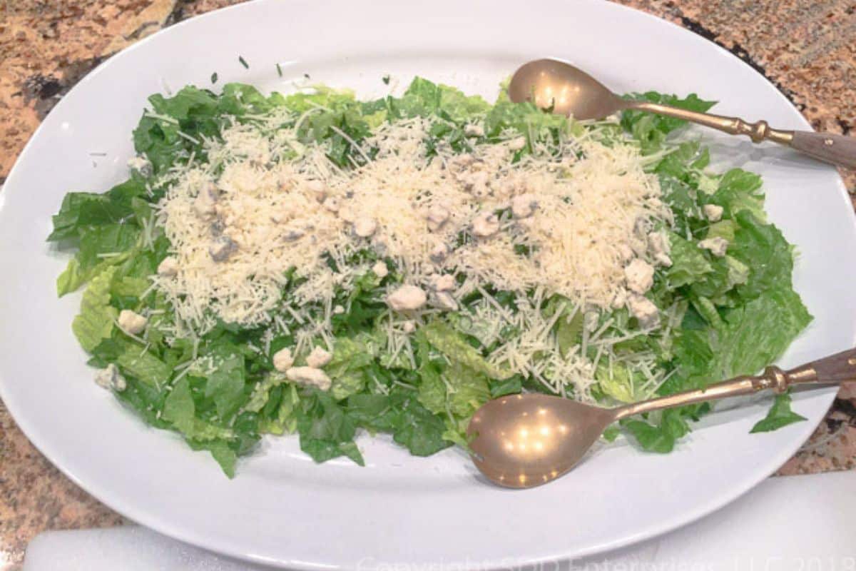 green salad with romano cheese on a serving platter with serving tongs.