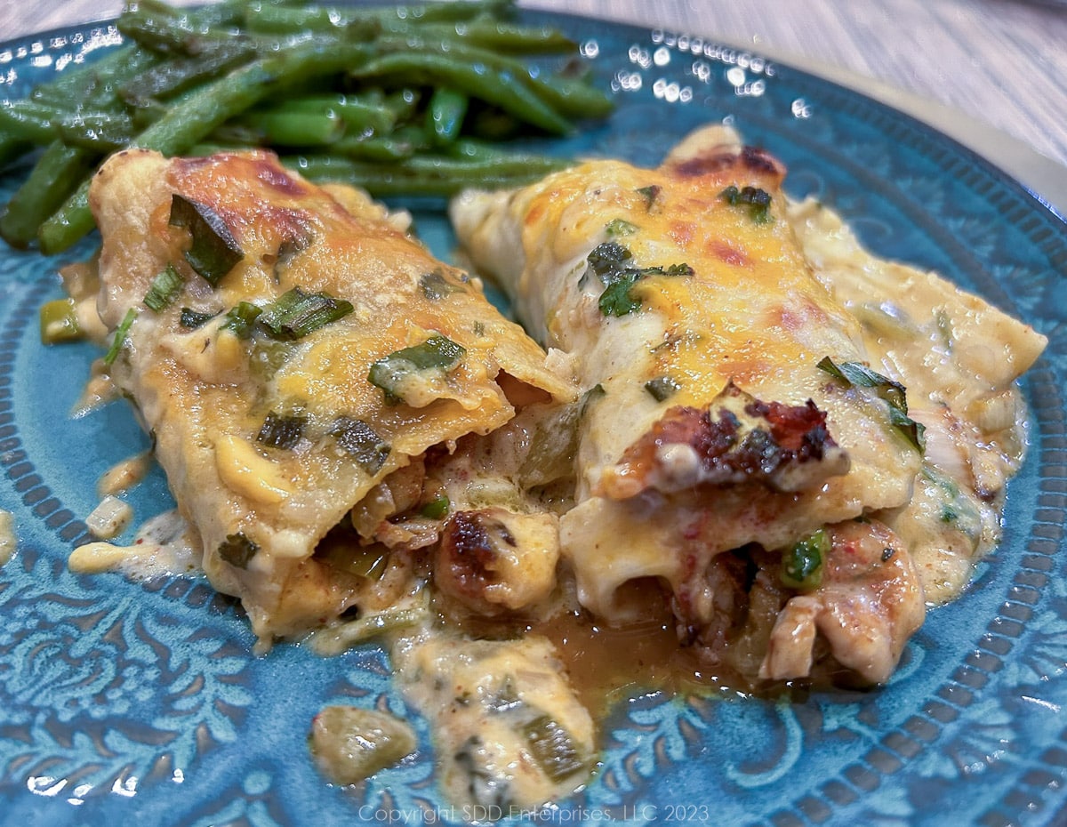 Crawfish enchiladas on a blue green plate with green beans.