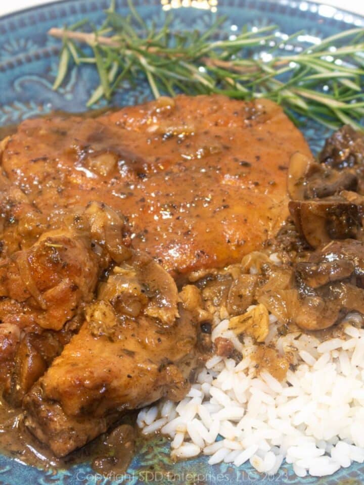 Smothered Pork Chops over rice and gravy with garnish on a blue green plate.