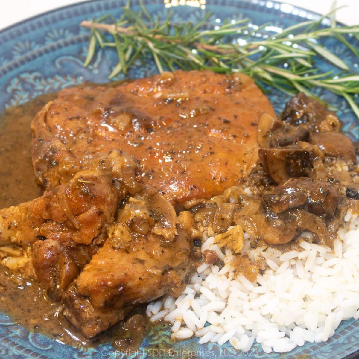 Smothered Pork Chops with gravy over rice on a blue green plate with garnish.