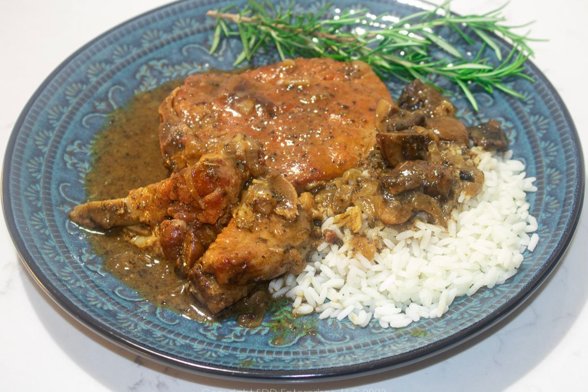 Smothered Pork Chops with gravy over rice on a blue green plate with garnish.