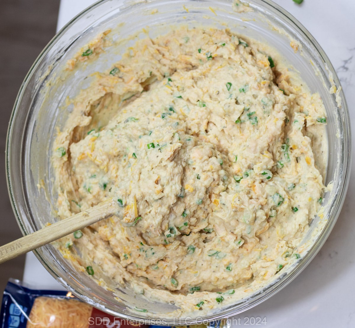 Mixed mashed potatoes and seasonings in a glass bowl.