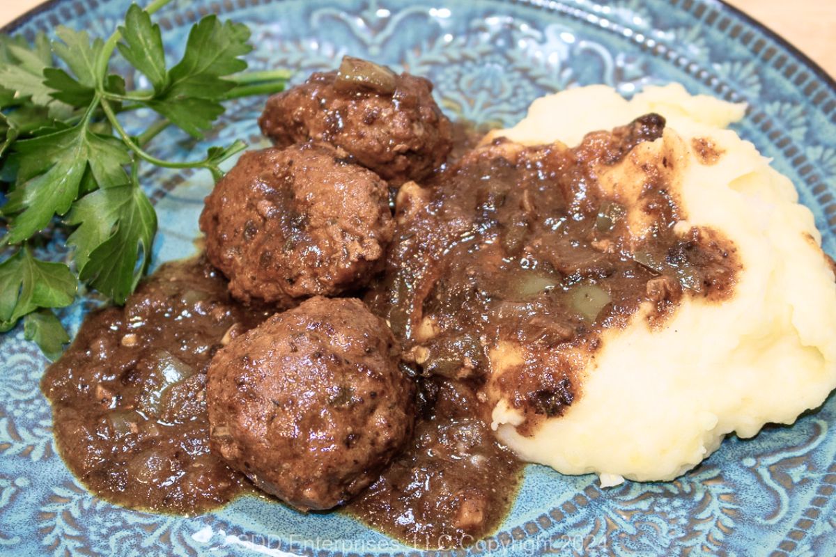 Cajun Meatballs in Brown Gravy on a blue green plate with mashed potatoes and garnish.