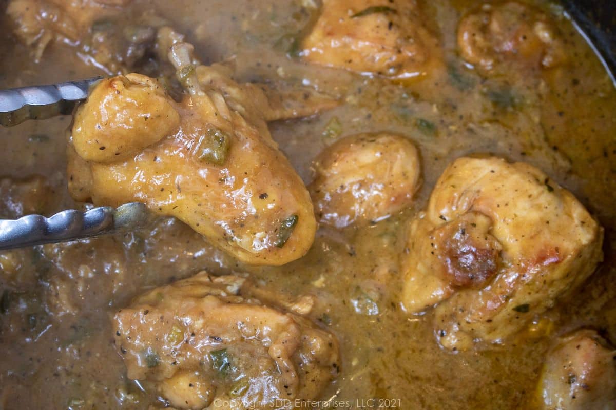 Holding a piece of chicken over a pot of Smothered Chicken. 