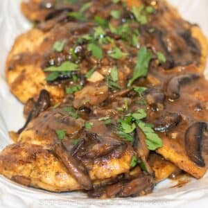 Chicken Marsala with parsley garnish on a white serving platter.