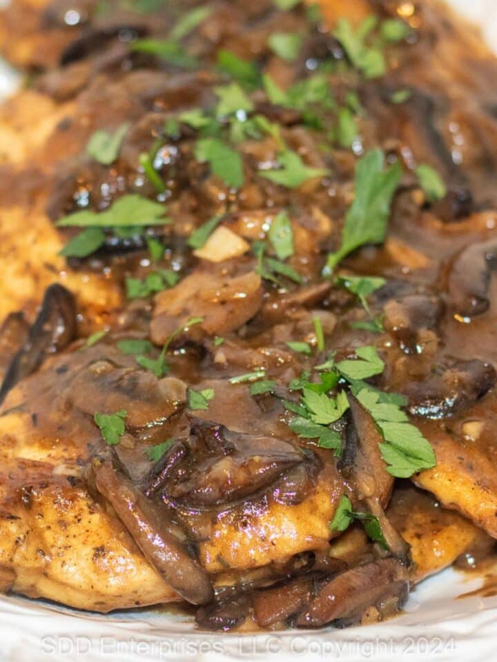 Chicken Marsala with parsley garnish on a white serving platter.