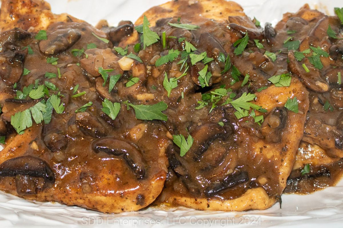 Chicken Marsala garnished with parsley on a white serving platter.