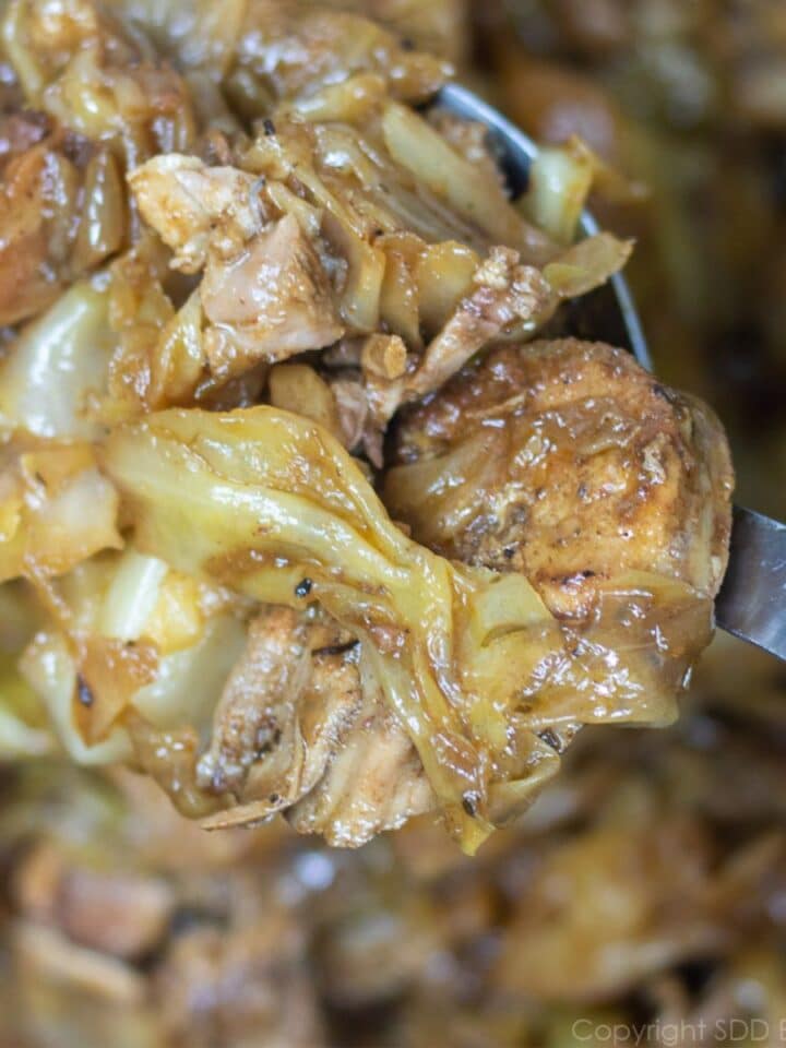 Smothered Cabbage with Pork on a serving spoon over a Dutch oven.