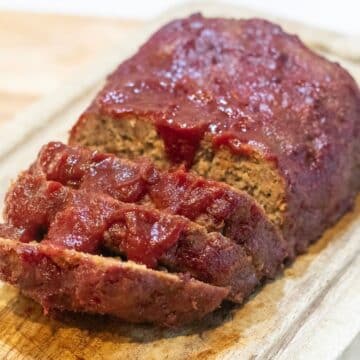 Meatloaf with red glaze, sliced on a cutting board.