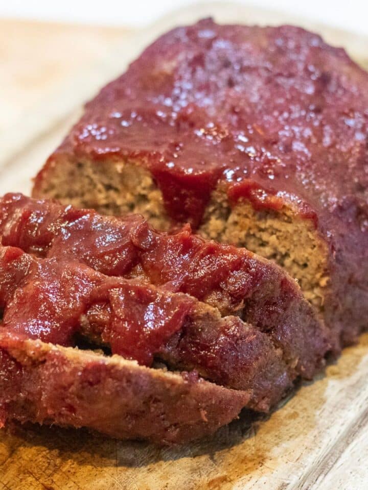 Meatloaf with red glaze, sliced on a cutting board.