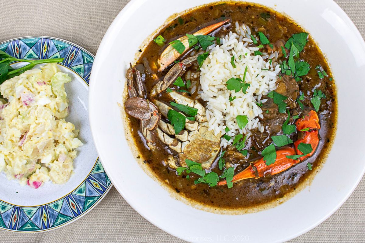 A bowl of Seafood Gumbo with rice and  a side of Potato Salad.