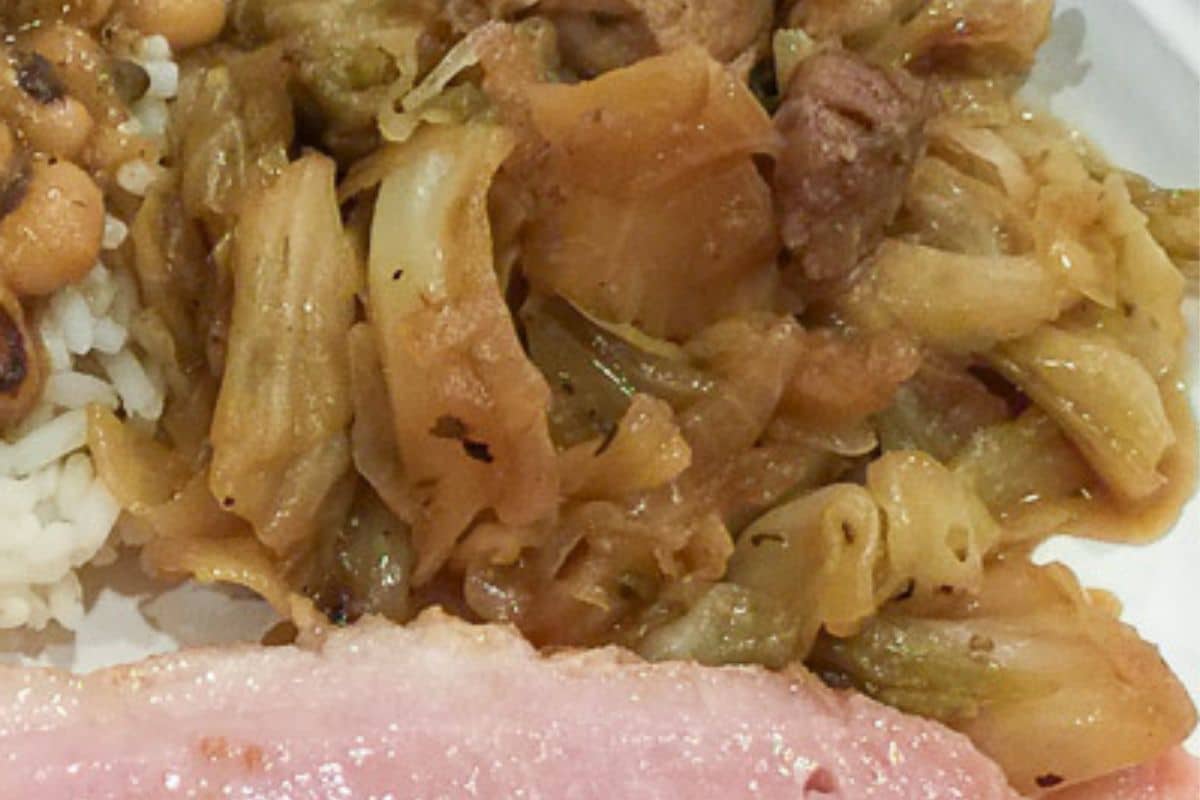 Smothered Cabbage with Pork served with ham and black-eyed peas on a white plate.