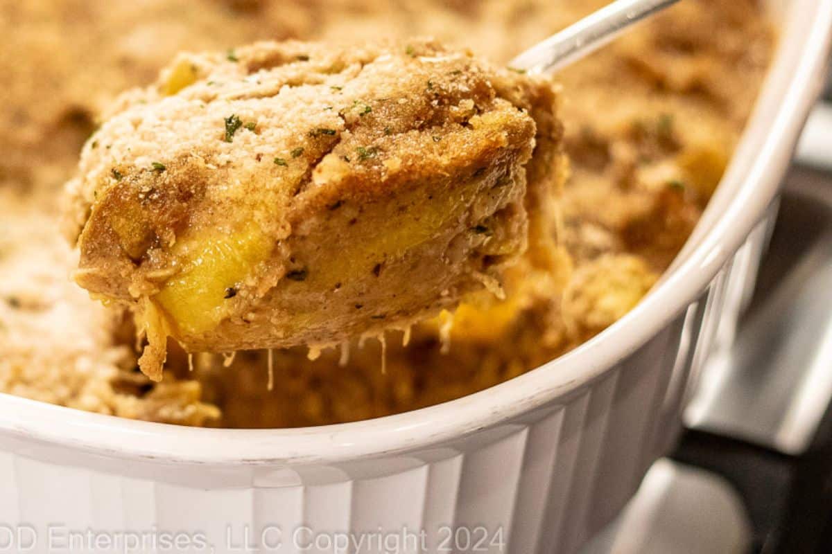 Yellow Squash Casserole on a serving spoon over a baking dish.