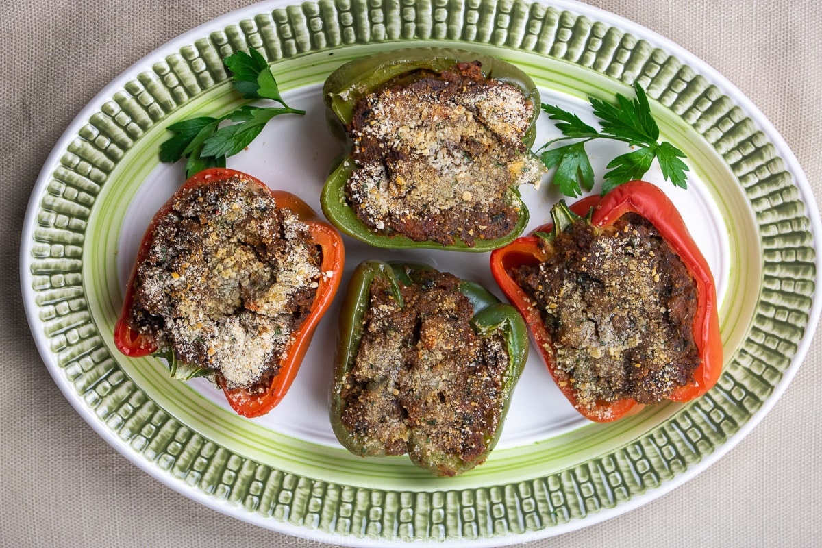 Four stuffed bell peppers on n an oval platter with garnish.