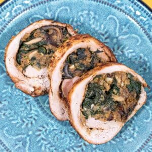 Three slices of stuffed pork tenderloin on a green blue plate.
