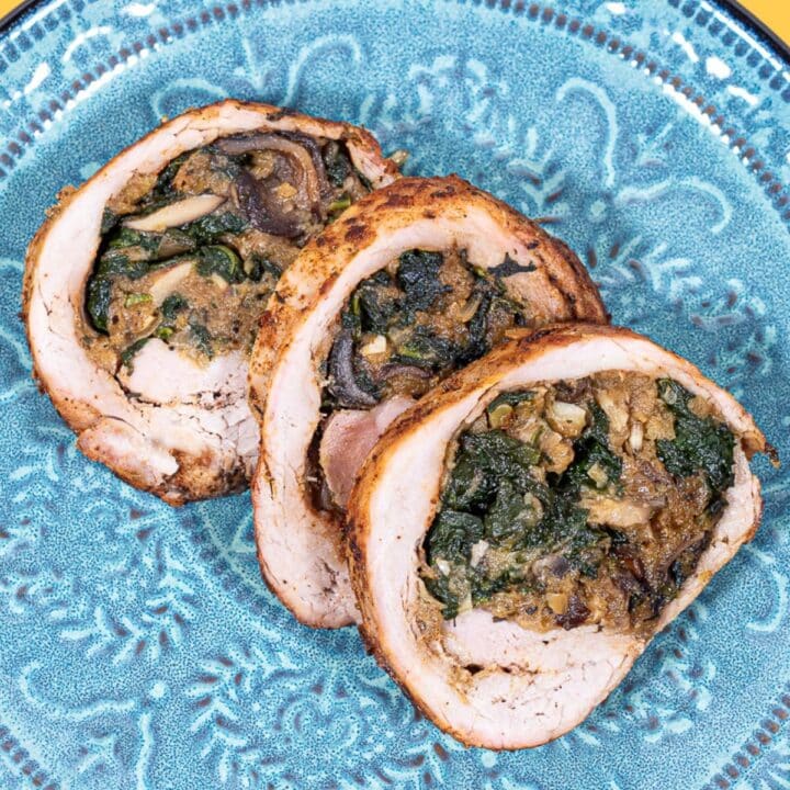 Three slices of stuffed pork tenderloin on a green blue plate.