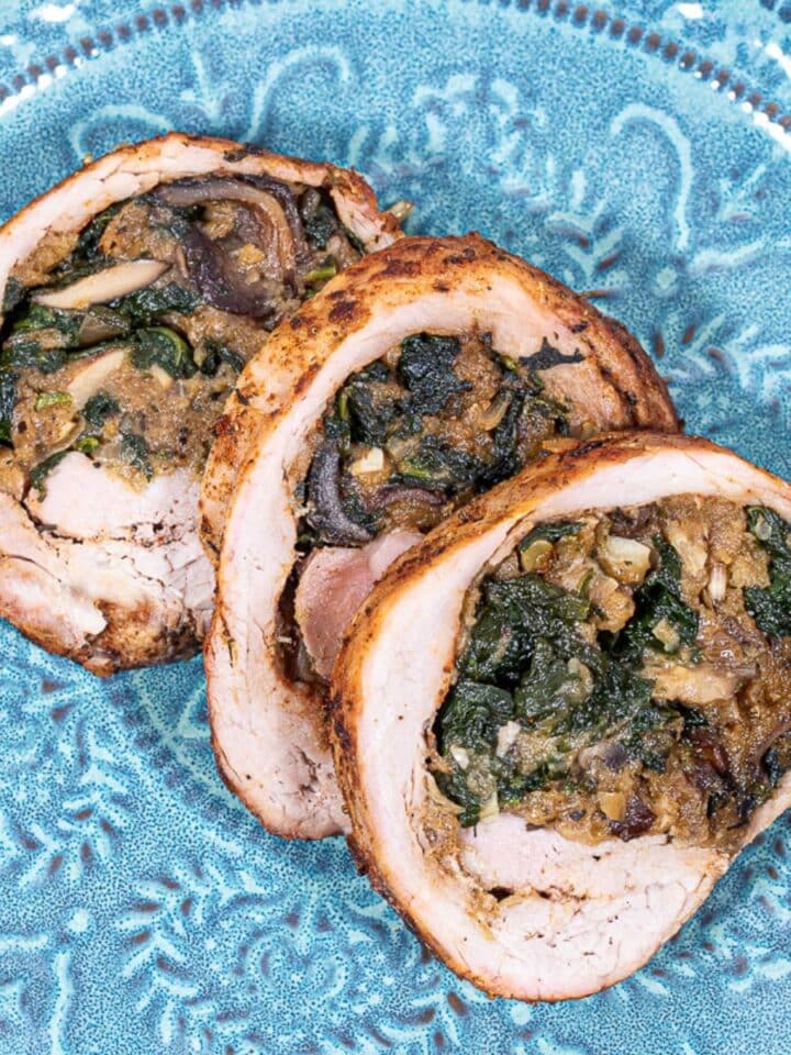 Three slices of stuffed pork tenderloin on a green blue plate.