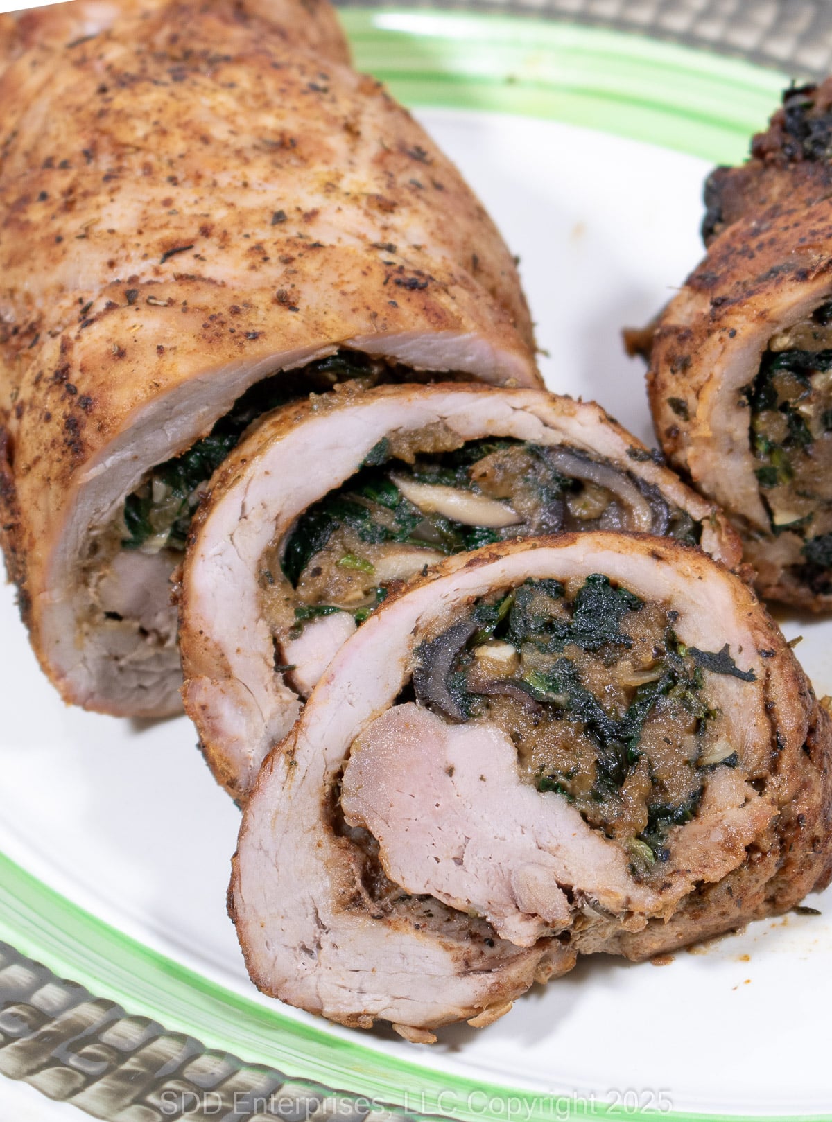 Sliced Stuffed Pork Tenderloin on a green and white serving platter.