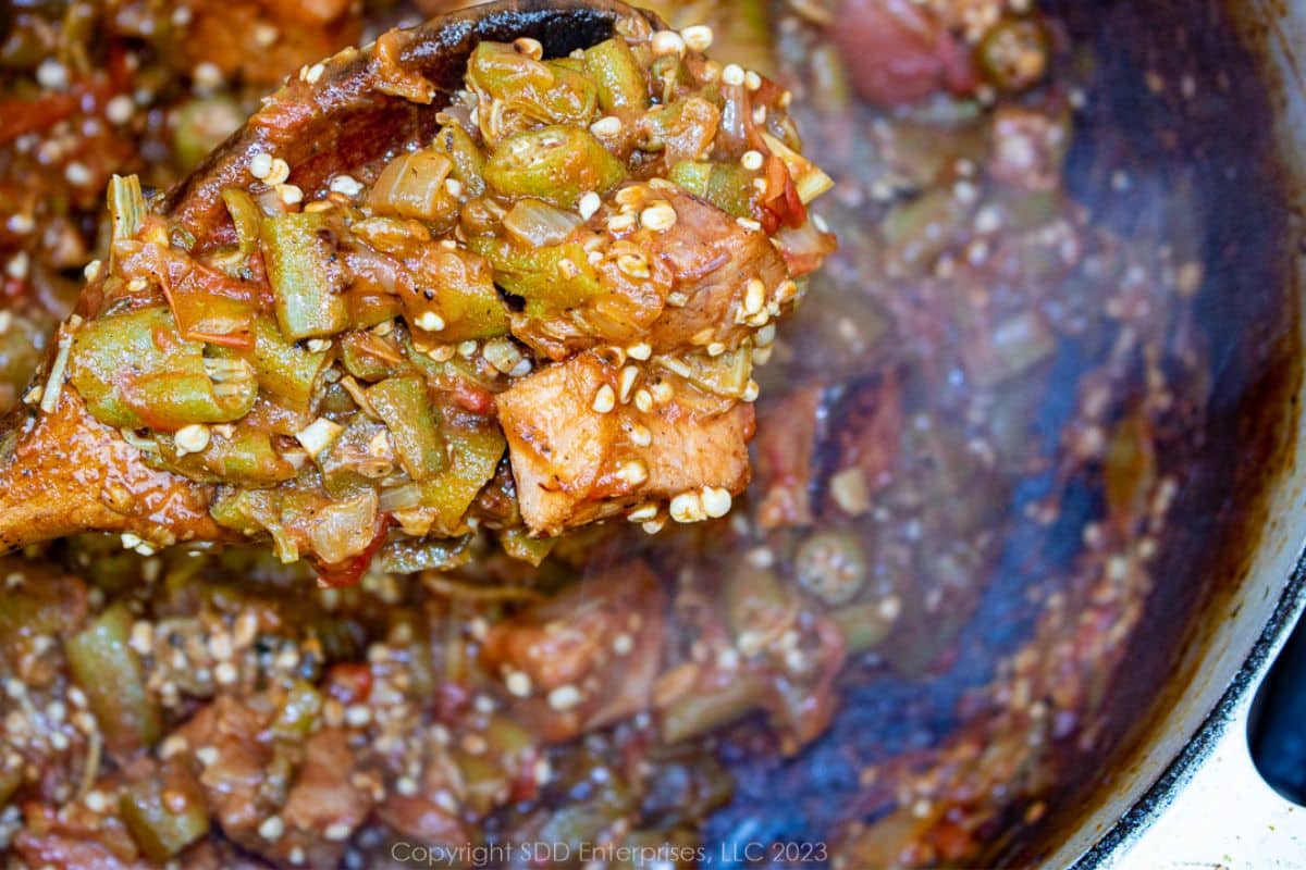 Smothered Okra on a spoon over a Dutch oven.